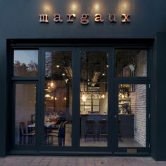 the outside of a restaurant with large glass doors and lights on it's windows