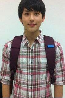 a young man with a backpack standing in front of a white wall and looking at the camera