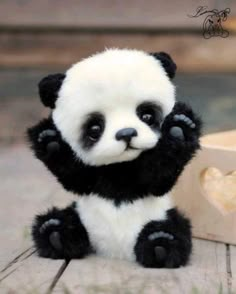 a small stuffed panda bear sitting next to a wooden box with its paws in the air