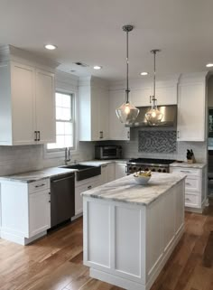 a kitchen with white cabinets and an island in the middle of the room is lit by two pendant lights