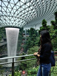 a woman standing in front of a waterfall looking at the water from inside a building