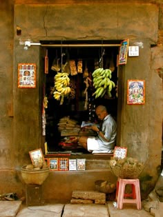 a man sitting in front of a store with bananas hanging from it's windows