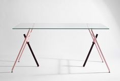 a glass table with two wooden legs and a pink base on the top, in front of a white wall