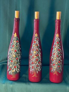 three red wine bottles with christmas trees painted on the sides and gold trimmings