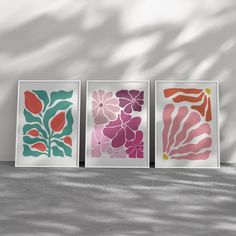 three framed art prints in different shades of pink, orange and green on a wall