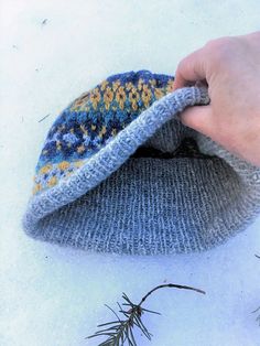 someone is holding a knitted hat in the snow, with needles sticking out of it