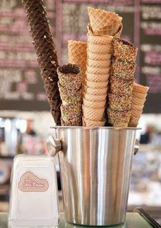 ice cream cones in a bucket with sprinkles and chocolate on the side