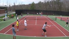 a group of people playing tennis on a red and green court with trees in the background