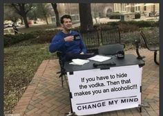 a man sitting at a table with a sign on it that says change my mind if you have to hide the vodka then that makes you an alcoholic