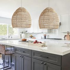 two hanging lights above an island in a kitchen with white counter tops and gray cabinets