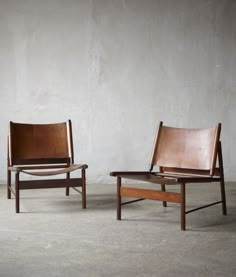 two chairs sitting next to each other in front of a white wall and concrete floor