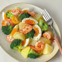 a white plate topped with shrimp, potatoes and broccoli next to a fork