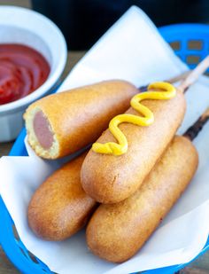 two hot dogs with mustard and ketchup on a blue plate next to a bowl of ketchup