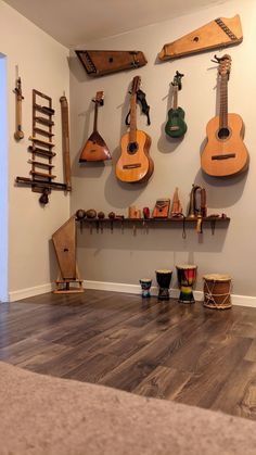 guitars and musical instruments are hanging on the wall in a room with hard wood flooring