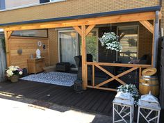 a patio covered in wooden furniture next to a brick building with white flowers on it