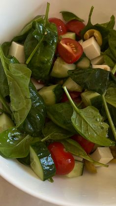 a white bowl filled with spinach, cucumber and tomatoes