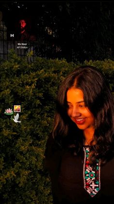 a woman standing in front of a bush smiling at the camera