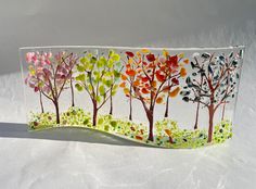 a handmade glass block with trees painted on the front and sides, sitting on a white surface