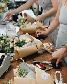 several women are working on flower arrangements at a table with scissors and flowers in vases