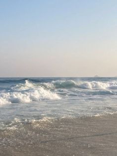 two people walking along the beach with surfboards in hand and waves crashing on the shore