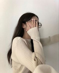 a woman wearing glasses covers her face with her hands as she leans against a wall