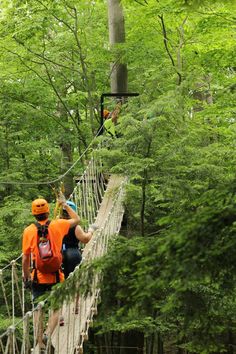 two people walking across a rope bridge in the woods with backpacks on their backs