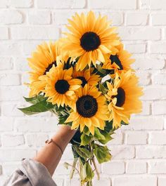 a person holding a bouquet of sunflowers in front of a brick wall