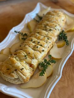 a long piece of bread with herbs on it sitting on a white plate next to sliced apples