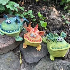 three small ceramic monsters sitting on some rocks