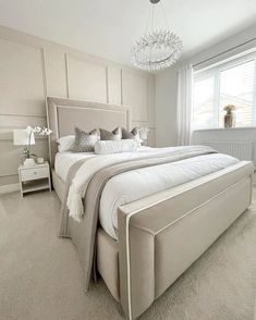 a large white bed sitting in a bedroom next to a window on top of a carpeted floor