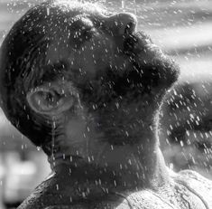 a black and white photo of a man's face with rain falling down on him