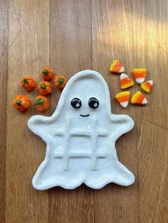 a white ghost shaped plate with candy on the floor next to it and pumpkins