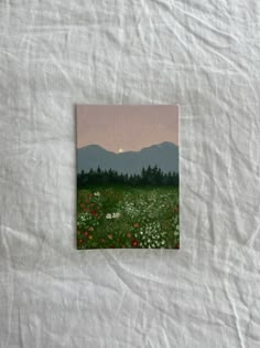 a painting on a white sheet with mountains in the background and wildflowers all around