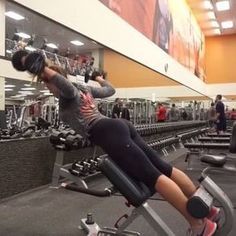 a woman doing exercises on an exercise bike in a gym with other people working out