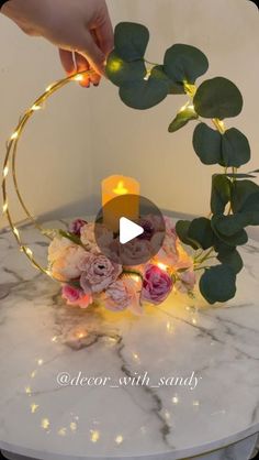 a person is holding a candle in front of a flower arrangement on a marble table