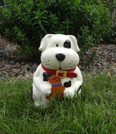 a white dog figurine sitting in the grass with a red collar around it's neck