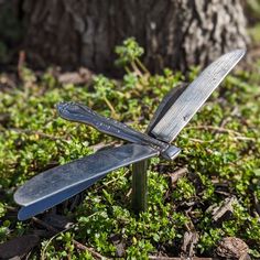 two knives sitting on top of each other in the grass next to a small tree