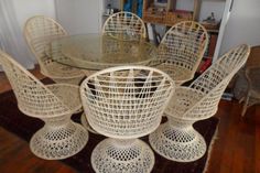 a glass table with white wicker chairs and a rug on the floor in front of it