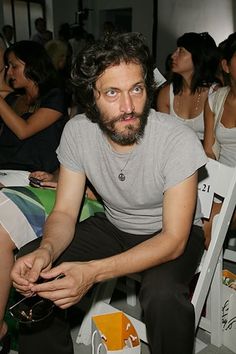 a man sitting in front of a group of people at a fashion show with his hands on his hips