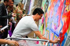 a man is pushing a shopping cart in front of a wall with graffiti on it