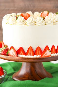 a white cake topped with strawberries on top of a wooden platter next to a bowl of fruit