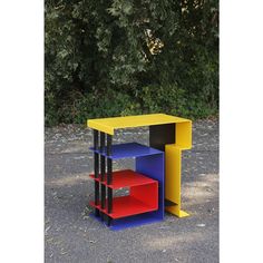 a multicolored book shelf sitting in the middle of a parking lot next to trees