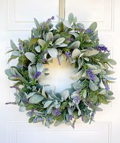 a wreath with purple flowers and green leaves hangs on the front door's white door