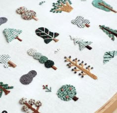 a close up of a cross stitch pattern on a piece of cloth with trees and leaves