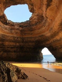 a person walking on the beach in front of a cave