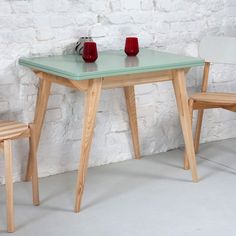 a table and two chairs in front of a white brick wall with red vases on it