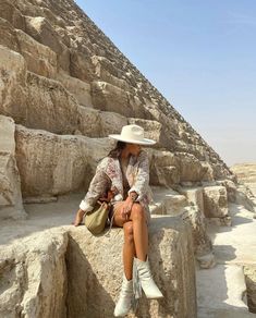 a woman sitting on top of a stone wall next to a large pyramid in the desert