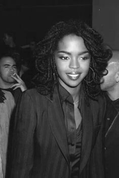 a black and white photo of a woman with long curly hair in a suit smiling at the camera