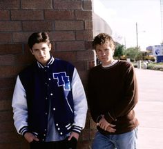 two young men leaning against a brick wall