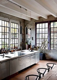 an industrial style kitchen with stainless steel appliances and large windows, along with wooden flooring